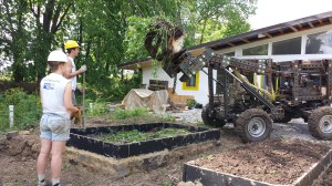 Emily Dixon (left) and Graham Coffman stand by as Marcin Jakubowski dumps soil into the raised garden beds using the OSE tractor, "LifeTrac."